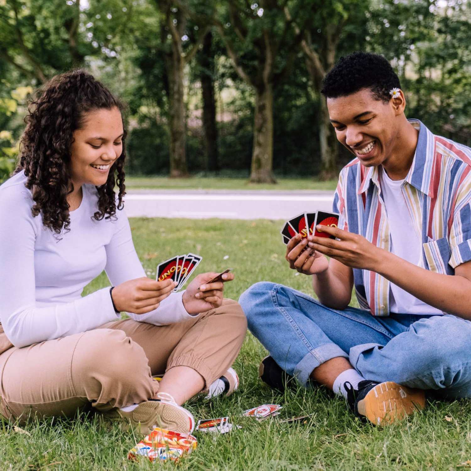 Two friends play uno together cross-legged in the park.