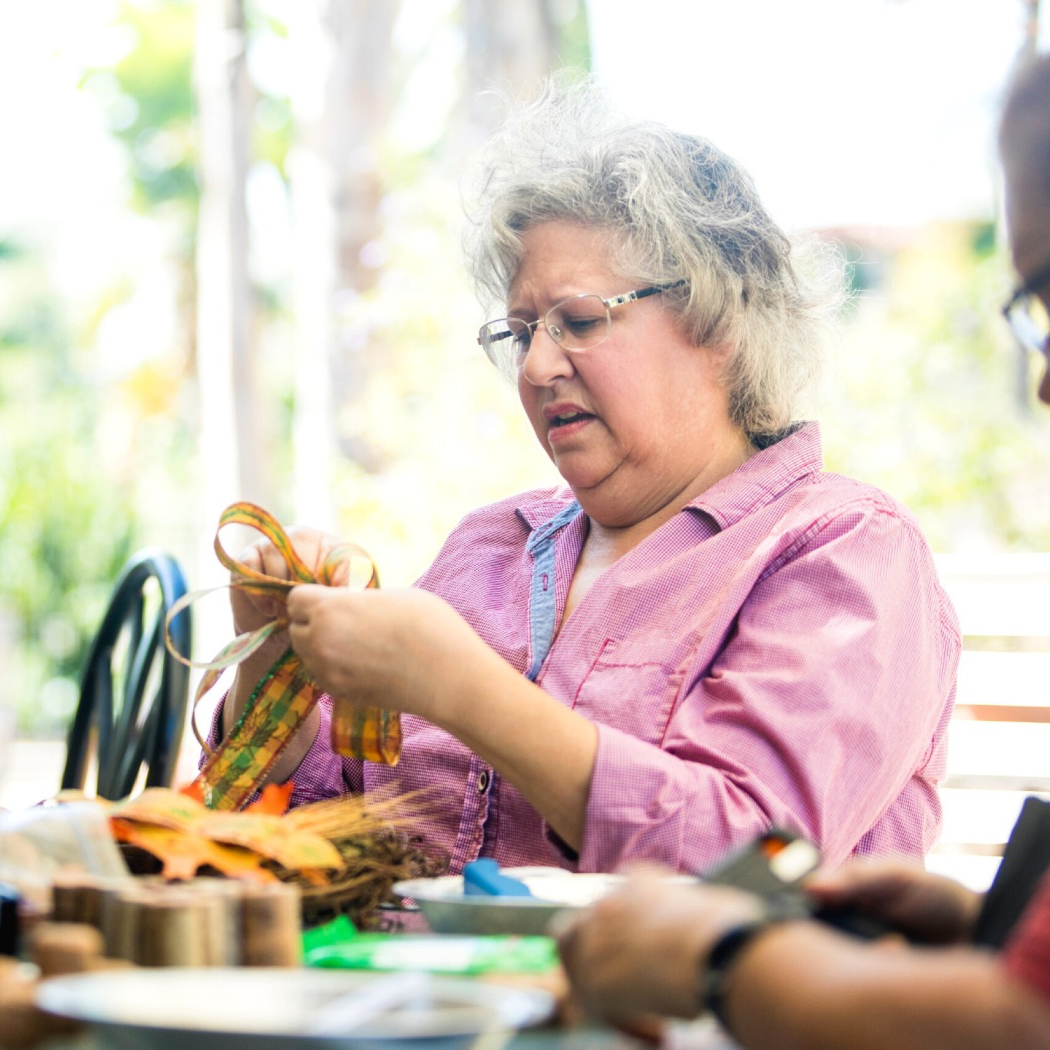 An older woman folds over ribbon while making crafts with a client.