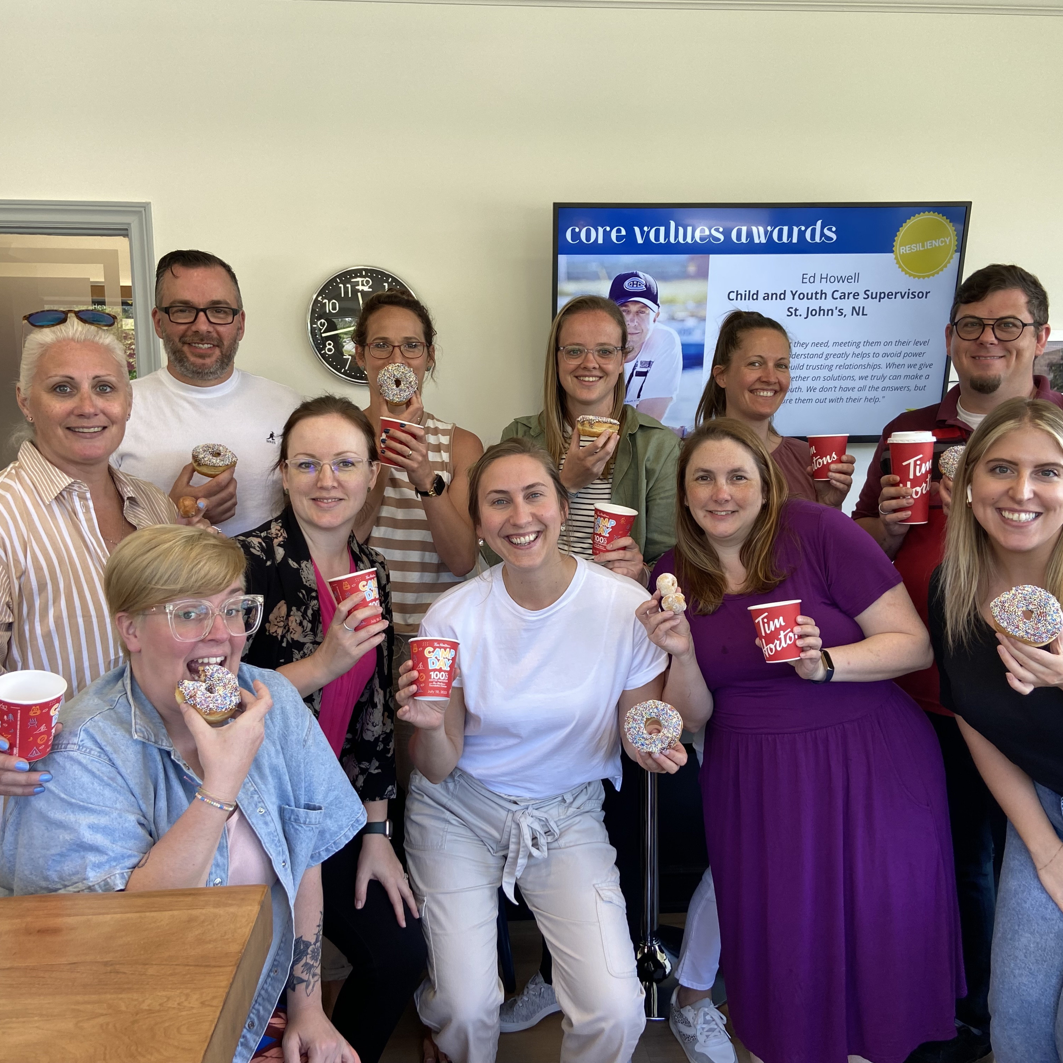 Staff members smiling while enjoying donuts and coffee.